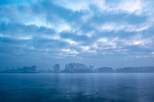Hazy winter landscape of a frozen lake with trees on the shore, Stankow, Poland