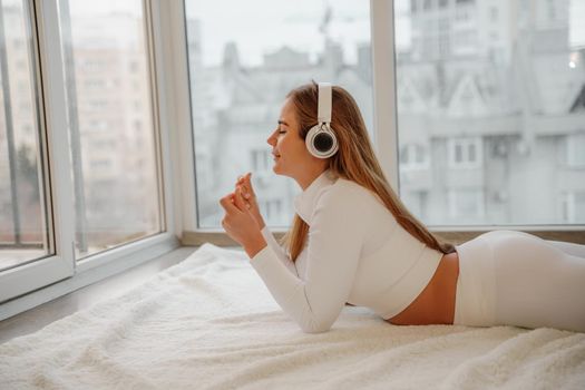 Side view portrait of relaxed woman listening to music with headphones lying on carpet at home. She is dressed in a white tracksuit