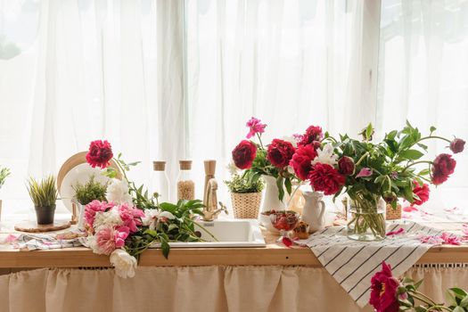 The kitchen countertop is decorated with peonies. The interior is decorated with spring flowers. Pink peonies and sweet cupcakes on a wooden countertop. Interior details