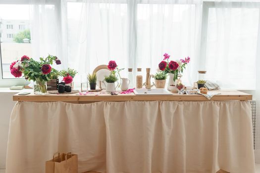 The kitchen countertop is decorated with peonies. The interior is decorated with spring flowers. Pink peonies and sweet cupcakes on a wooden countertop. Interior details