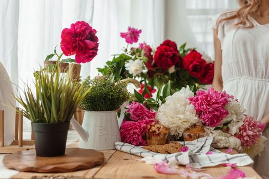 The kitchen countertop is decorated with peonies. The interior is decorated with spring flowers. Pink peonies and sweet cupcakes on a wooden countertop. Interior details