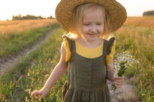A little blonde girl in a straw hat walks in a field with a bouquet of daisies. The concept of walking in nature, freedom and an eco-friendly lifestyle