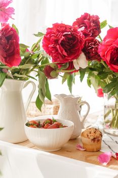 The kitchen countertop is decorated with peonies. The interior is decorated with spring flowers. Pink peonies and sweet cupcakes on a wooden countertop. Interior details