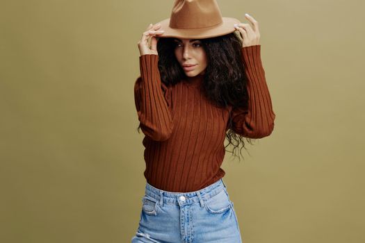 Fashion Offer. Seasonal Sale concept. Confident stylish curly Latin female in casual wear, smiling, look at the left, holding hand on hat, isolated green background. Mock up copy space free place ad.