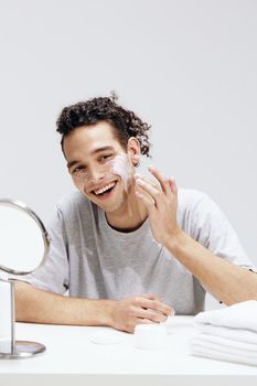 handsome guy sit in front of the mirror, facial skin care light background. High quality photo