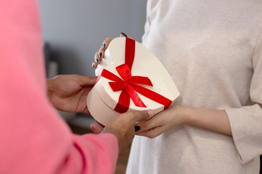 A guy in a pink jumper gives a girl in a white dress a white box in the shape of a heart. close-up