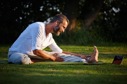 Shot of a mature man looking at online instructions on his tablet while doing yoga.