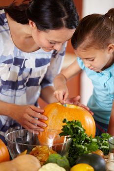 A happy young mother helping her daughter to carve a pumpkin in the kitchen.