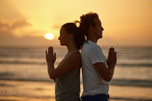 Shot of a couple doing yoga on the beach at sunset.