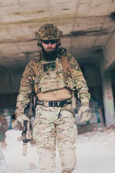 A bearded soldier in a special forces uniform walks through an abandoned building after a successful mission. Selection focus. High-quality photo