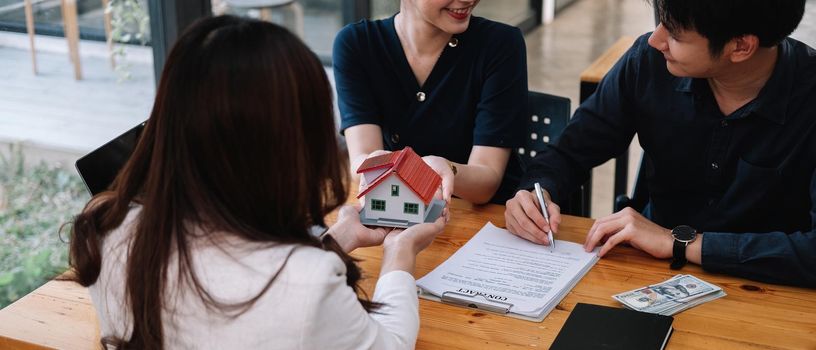 Real estate agent offer hand for customer sign agreement contract signature for buy or sell house. Happy asian couple signing a contract together at office. Real estate contact agreement concept.