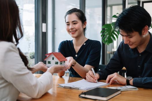 Real estate agent offer hand for customer sign agreement contract signature for buy or sell house. Happy asian couple signing a contract together at office. Real estate contact agreement concept.