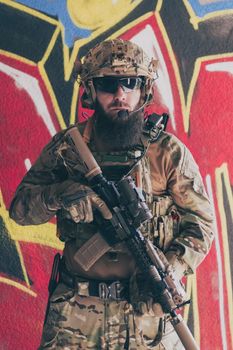 A bearded soldier in a special forces uniform stands in front of a drawn wall with a rifle in his hand. Selective focus. High-quality photo