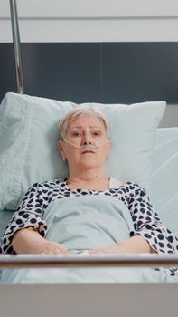 POV of ill patient using online video call for telehealth chat in hospital ward. Retired woman with disease looking at camera and talking on conference for remote communication in bed