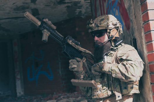 A bearded soldier in special forces uniform in a dangerous military mission, refile his weapon while hiding from the wall. Selective focus. High-quality photo