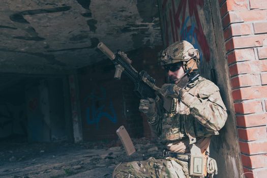 A bearded soldier in special forces uniform in a dangerous military mission, refile his weapon while hiding from the wall. Selective focus. High-quality photo