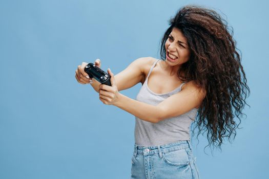 ONLINE GAME AD CONCEPT. Furious beautiful curly Latin lady hold game pad near face, ready to play cool RPG, look at side. Gaming accessories brands ad. Studio shoot isolated blue background
