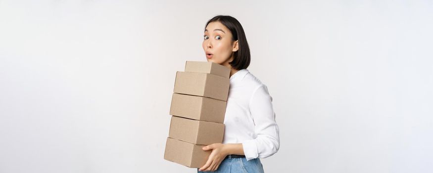 Portrait of young asian woman holding boxes, carry delivery goods. Korean female entrepreneur assemble order, standing voer white background.