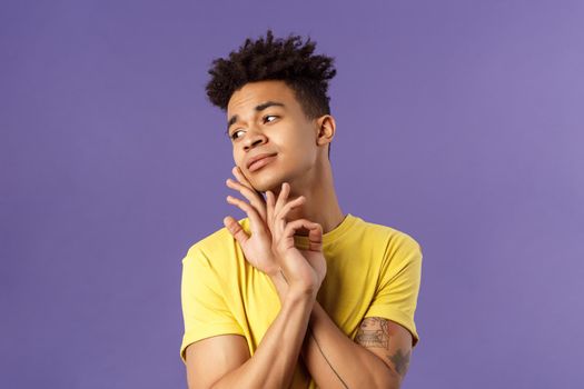 Close-up portrait of glamour beautiful young queer guy with dreads, standing in feminine model pose, gently touching face and looking away sensual, standing purple background.