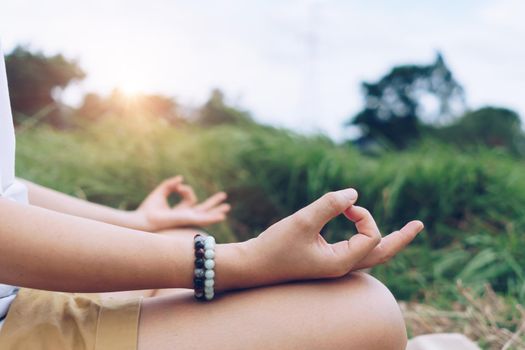 Woman practicing yoga lesson, breathing, meditating exercise, outdoor in grass field. Well being, wellness concept