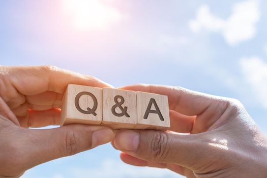 Q and A alphabet on wooden cube in hand hold with background. Question and answer meaning concept.