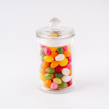 glass jar filled with candy and caramel with the lid closed on white background.