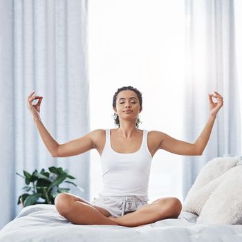 Shot of an attractive young woman meditating while sitting on her bed in the morning.