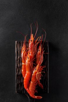 Top view of cooked whole red shrimps on wooden serving board on black background with copyspace. Vertical image