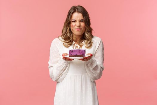 Holidays, spring and party concept. Portrait of excited and pleased blond female in white dress, holding piece of delicious cake and grimacing satisfied, cant wait to have bite of tasty dessert.