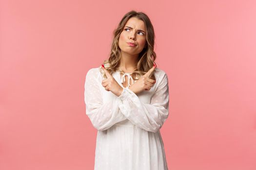 Beauty, fashion and women concept. Girl having problem with picking, making serious decision. Attractive blond woman look up thoughtful, smirk and grimacing, pointing sideways, point left and right.