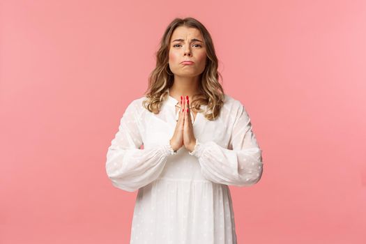 Portrait of hopeful clingy girlfriend, blond girl begging for favour in white dress over pink background, sobbing make cute eyes, pleading or praying, say please, want something badly.