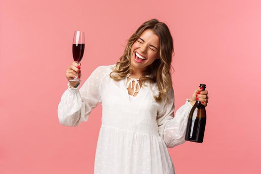 Holidays, spring and party concept. Portrait of excited and emotive good-looking blond girl dancing and celebrating, having fun saying yeah singing closed eyes, hold glass wine and bottle.