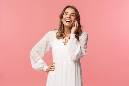 Portrait of carefree good-looking girl with blond short hair, wear white dress, laughing happy as talking on phone, hear funny joke, have conversation using mobile, hold smartphone and chuckle.