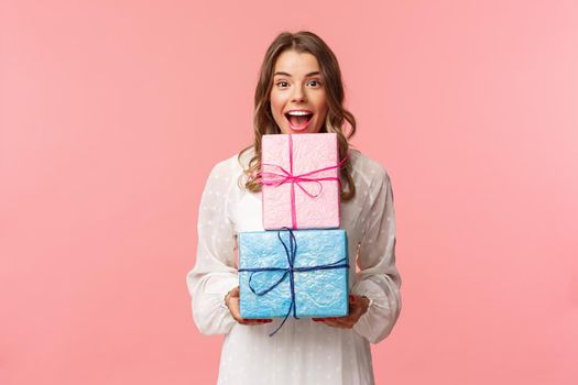 Holidays, celebration and women concept. Portrait of happy cheerful girl likes celebrating birthday and receive presents, holding two gift boxes and smiling camera, pink background.