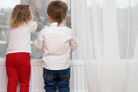 Little boy and girl are standing near the window. Expectation, hope, dream. copy space, peace.