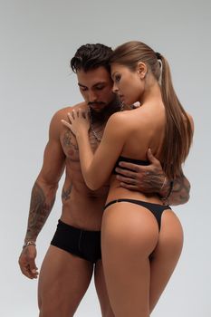 Muscular tattooed man embracing slim topless woman in panties on gray background