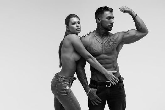 Black and white tattooed shirtless man and seductive topless woman looking away