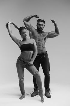 Black and white side view of topless woman and shirtless man looking at camera against gray background