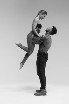 Black and white side view of topless woman and shirtless man looking at camera against gray background