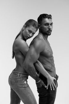 Black and white side view of topless woman and shirtless man looking at camera against gray background