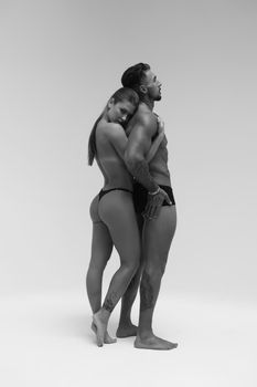 Black and white side view of topless woman and shirtless man looking at camera against gray background