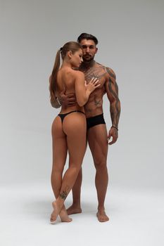 Muscular tattooed man embracing slim topless woman in panties on gray background