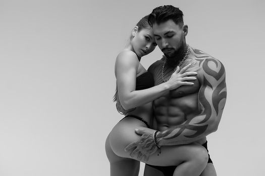 Black and white tattooed shirtless man and seductive topless woman looking away