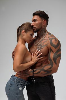 Muscular tattooed man embracing slim topless woman in panties on gray background