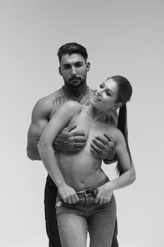 Black and white side view of topless woman and shirtless man looking at camera against gray background