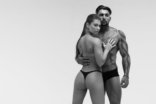 Black and white tattooed shirtless man and seductive topless woman looking away