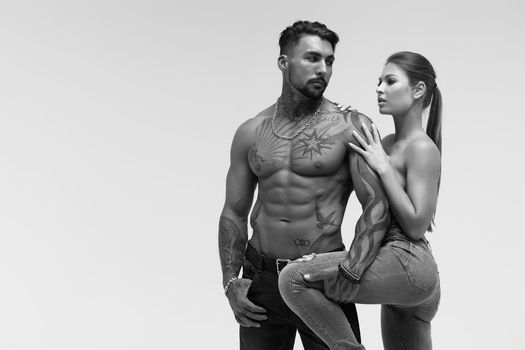 Black and white tattooed shirtless man and seductive topless woman looking away