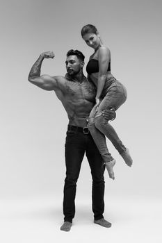 Black and white side view of topless woman and shirtless man looking at camera against gray background