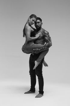 Black and white side view of topless woman and shirtless man looking at camera against gray background