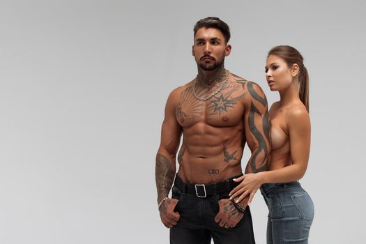 Muscular tattooed man embracing slim topless woman in panties on gray background